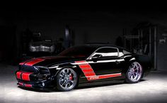 a black sports car with red stripes parked in a garage at night, lit up by the headlights