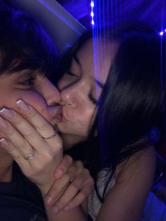 a man and woman kissing each other in front of a blue wall with lights on it