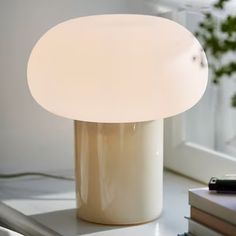 a white table lamp sitting on top of a desk next to a book and pen