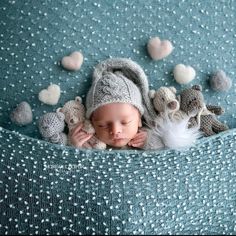 a newborn baby wearing a knitted hat and surrounded by stuffed animals is laying on a blue blanket