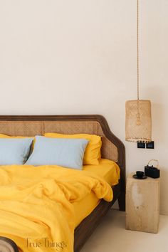 a bed with yellow sheets and blue pillows in a white room next to a lamp