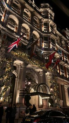 an ornate building lit up at night with christmas lights on the windows and flags flying in the wind