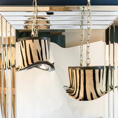 two zebra print lamps hanging from the ceiling in front of a white wall and mirror