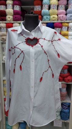 a white shirt with red beads on it in front of yarns and crochet