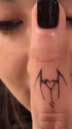 a woman is holding her finger up to the camera with a bat tattoo on it