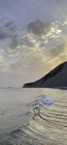 the sun is setting over the ocean with waves in the foreground and hills in the background