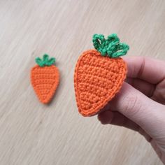 two crocheted carrots are being held by someone's hand on a table