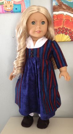 a doll with blonde hair wearing a blue dress and black shoes is standing on a shelf