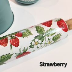 a strawberries rolling pin sitting on top of a table next to a blue cup