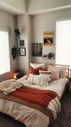 a bed with pillows and blankets on top of it in a bedroom next to two windows