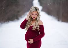 a pregnant woman standing in the snow with her hands on her head and wearing a red dress