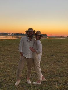 a man and woman standing next to each other in a field with the sun setting behind them