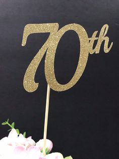 a cake topper with the number seventy on it and some flowers in front of it