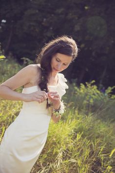 a woman in a white dress is standing in tall grass and looking at her cell phone