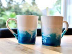 two coffee mugs sitting on top of a wooden table next to eachother