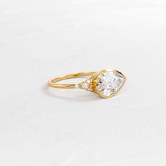 a yellow gold ring with an oval cut diamond in the center and two small diamonds on each side