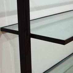 a glass shelf with black metal frame against a white wall