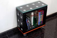 a black and orange shelf with books, bottles and cans on it's wheels