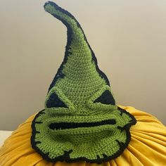 a crocheted green hat with black trim on top of a yellow pillow in front of a white wall