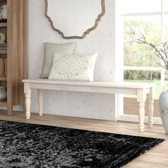 a white bench sitting in front of a window next to a book case and vase