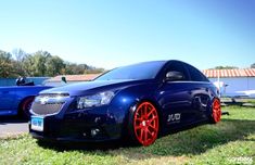 a blue car with red rims parked in the grass