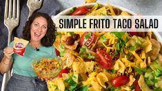 a woman holding a bag of taco salad next to a bowl of chips and a fork