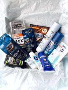 an assortment of men's grooming products in a white paper bag on top of a bed