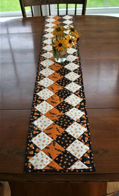 the table runner is decorated with orange and black quilted squares, polka dots, and daisies