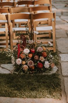 an arrangement of flowers sits on the ground in front of rows of empty wooden chairs