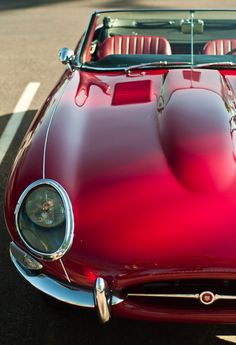 a red sports car parked in a parking lot with its hood up and the top down