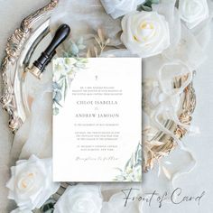 the wedding stationery is surrounded by white roses and greenery, along with an ornate silver frame