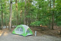 a green and white tent in the middle of a wooded area with trees on both sides