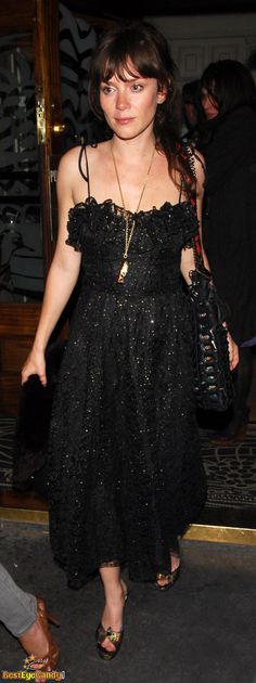 a woman wearing a black dress and holding a purse in her hand while walking into a building