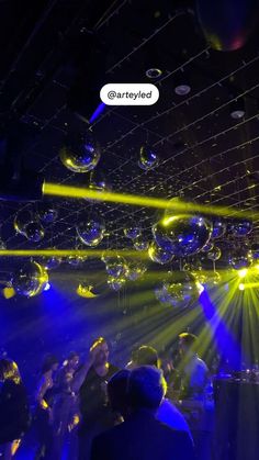 people are dancing at a party with bubbles floating in the air and lights shining down on them