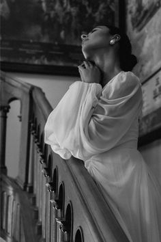 black and white photograph of woman in dress leaning on banister looking up at painting