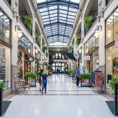 two people are walking down the middle of a shopping mall with lots of plants on display