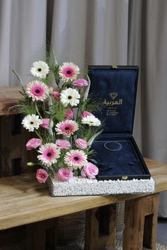 a bouquet of pink and white flowers sitting on a table next to an open box