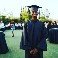 a man wearing a graduation cap and gown standing in front of tables with blue cloths