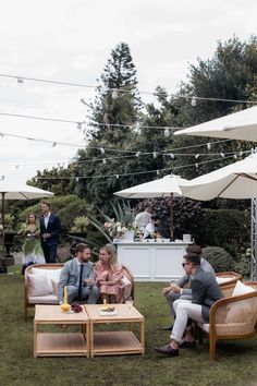 a group of people sitting on top of a grass covered field next to umbrellas