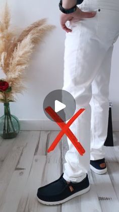 a person wearing white pants and black shoes standing next to a vase with red flowers