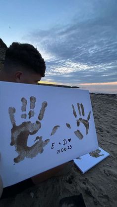 a young boy holding up a hand and footprints on a white paper with the ocean in the background