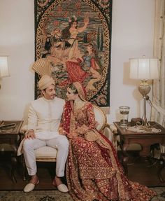 a bride and groom sitting on a chair in front of a tapestry