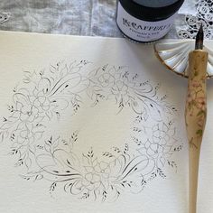 an inking technique is being used to create a floral wreath on white paper next to a paintbrush