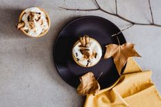 two cups of hot chocolate with whipped cream and cinnamon sprinkles on a black plate