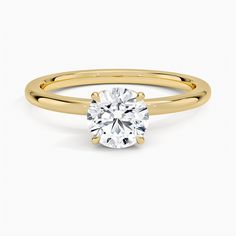 a yellow gold engagement ring with a round cut diamond in the center, on a white background