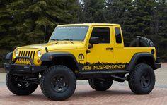 a yellow jeep with black tires parked in front of some trees and brick pavers