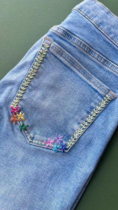 a pair of blue jeans with embroidered flowers on the back pocket and side zippers