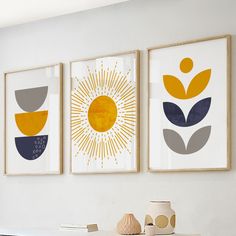 three framed art pieces hang on the wall above a table with vases and books