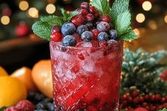 a red drink with berries and mint garnish on the rim surrounded by christmas decorations