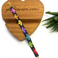 a wooden heart shaped box with a colorful beaded bracelet on it next to a plant